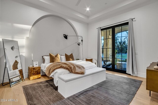 bedroom featuring access to outside, french doors, a raised ceiling, and light hardwood / wood-style floors