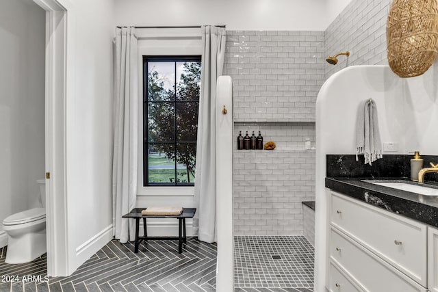 full bathroom featuring toilet, tile patterned flooring, a tile shower, and vanity