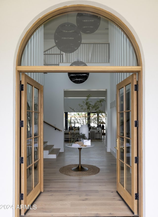 foyer entrance featuring light wood-style floors, french doors, stairway, and a towering ceiling