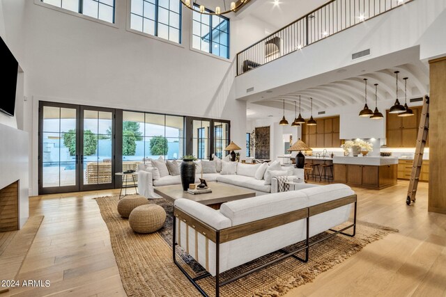 living room featuring high vaulted ceiling, light wood-type flooring, sink, an inviting chandelier, and french doors