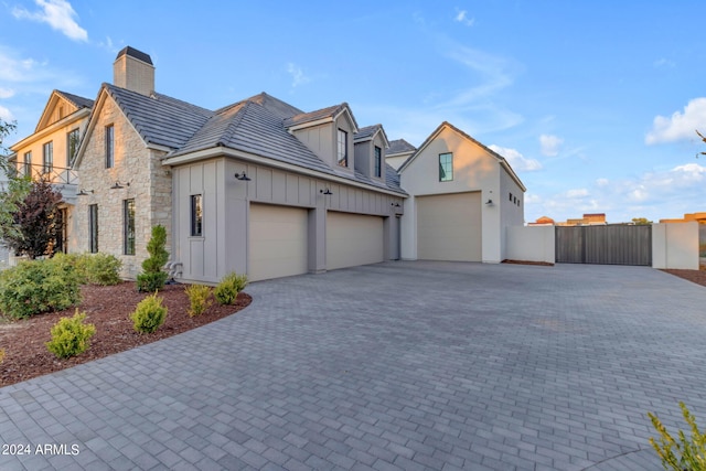 view of home's exterior with a garage, stone siding, decorative driveway, board and batten siding, and a chimney