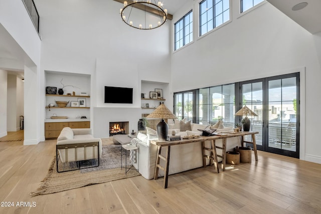 living room featuring light hardwood / wood-style floors, built in shelves, a towering ceiling, and an inviting chandelier