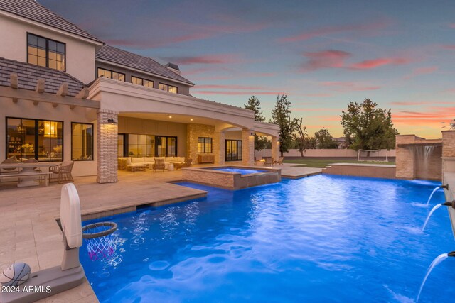 pool at dusk featuring a patio area, an in ground hot tub, and pool water feature