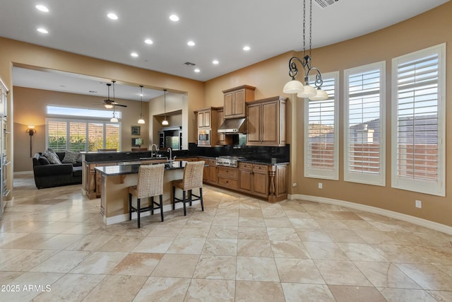 kitchen featuring ceiling fan, hanging light fixtures, a breakfast bar, a large island with sink, and decorative backsplash