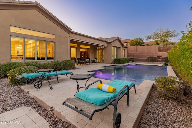 pool at dusk with a patio area and pool water feature