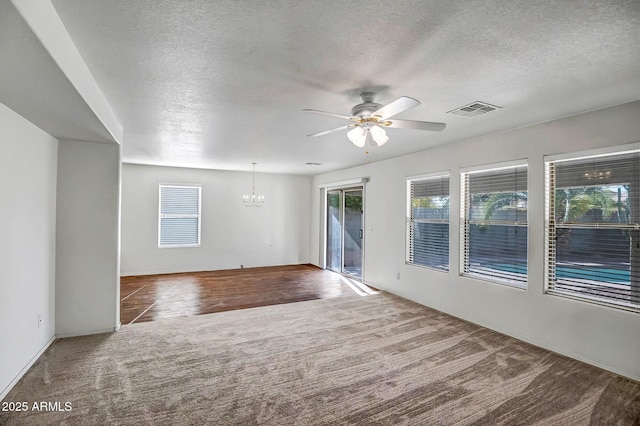 carpeted spare room with ceiling fan with notable chandelier, a textured ceiling, and a healthy amount of sunlight