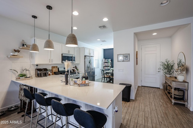 kitchen with stainless steel appliances, decorative light fixtures, white cabinetry, a kitchen breakfast bar, and kitchen peninsula