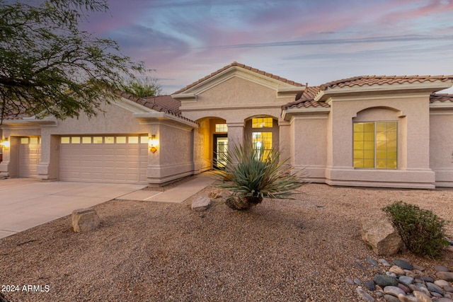 mediterranean / spanish-style house featuring an attached garage, a tiled roof, stucco siding, and driveway