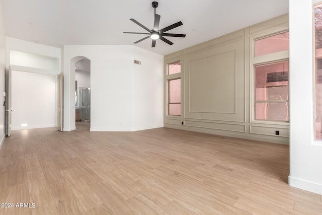 unfurnished room with arched walkways, baseboards, light wood finished floors, and a ceiling fan