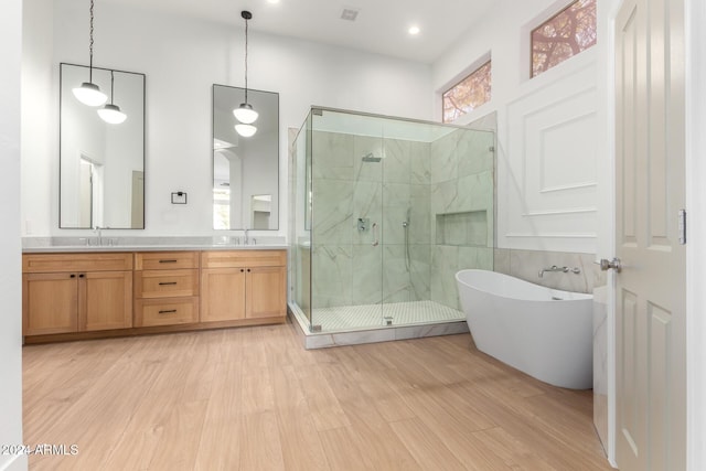 bathroom with a sink, a shower stall, double vanity, a freestanding bath, and wood finished floors