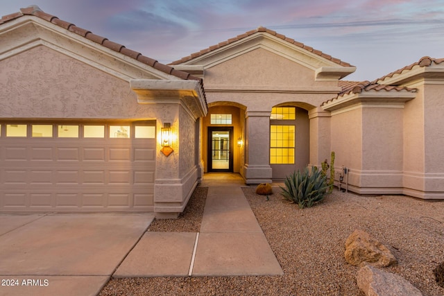property entrance with driveway, stucco siding, a garage, and a tile roof