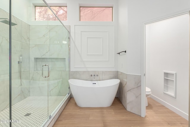 full bath featuring toilet, wood finished floors, a stall shower, a soaking tub, and tile walls