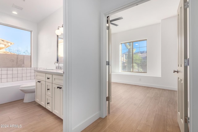 full bath featuring toilet, wood finished floors, a bath, baseboards, and vanity