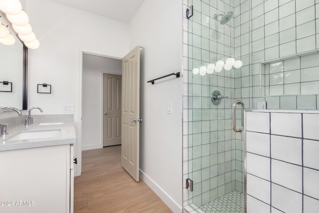 bathroom featuring double vanity, wood finished floors, a stall shower, and a sink