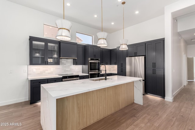 kitchen with light wood finished floors, stainless steel appliances, decorative backsplash, and light stone counters