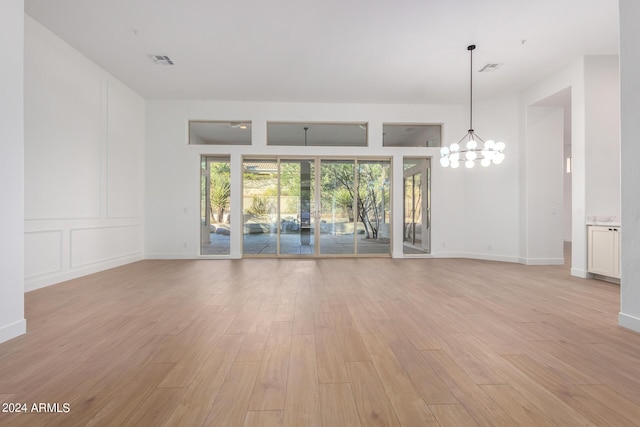 unfurnished living room featuring light wood-type flooring, baseboards, a chandelier, and visible vents