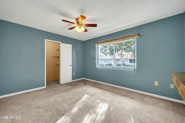 unfurnished bedroom with a textured ceiling, a walk in closet, ceiling fan, and carpet flooring