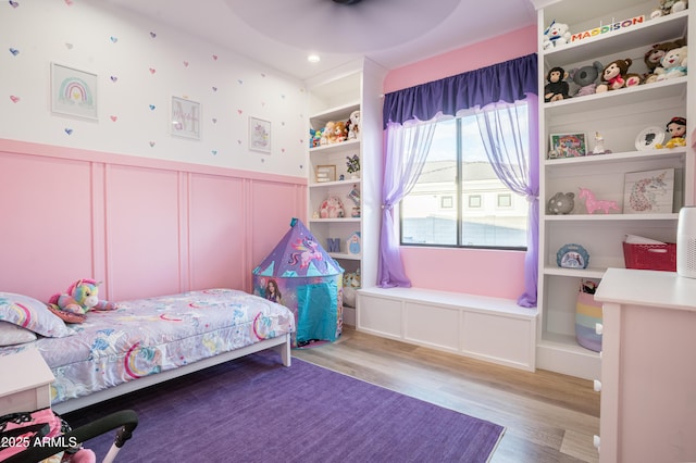 bedroom featuring wood finished floors, a decorative wall, and a wainscoted wall
