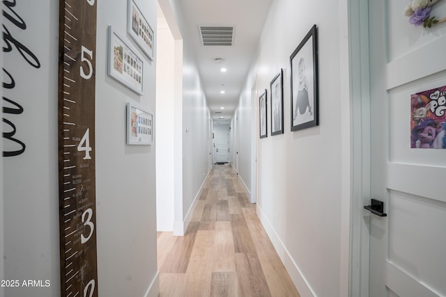 hallway with light wood finished floors, visible vents, and baseboards