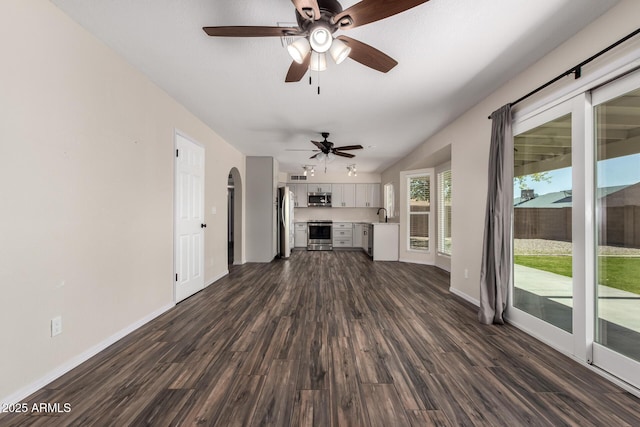 unfurnished living room featuring dark wood-type flooring, a ceiling fan, baseboards, and arched walkways