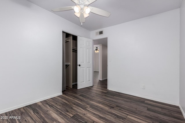 unfurnished bedroom featuring visible vents, baseboards, dark wood-type flooring, and a closet