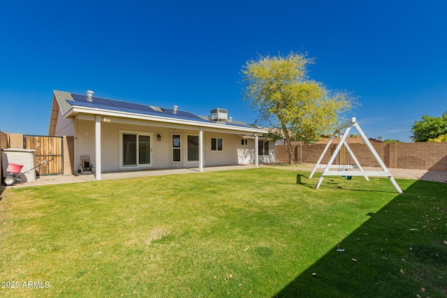 rear view of house with cooling unit, solar panels, a fenced backyard, a playground, and a patio area