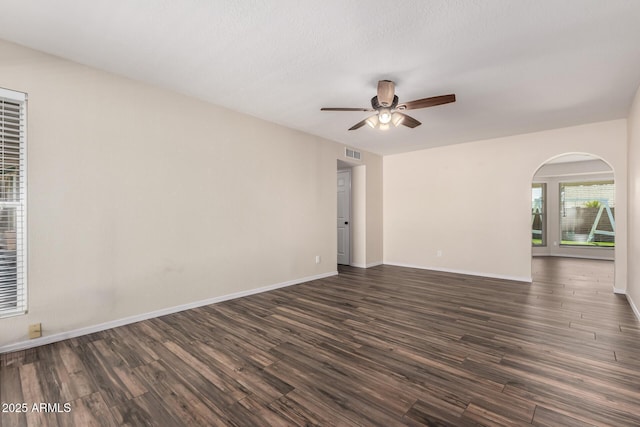 empty room featuring visible vents, baseboards, ceiling fan, arched walkways, and dark wood-style floors