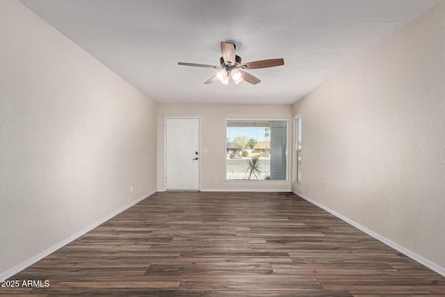 empty room with dark wood-style floors, a ceiling fan, and baseboards