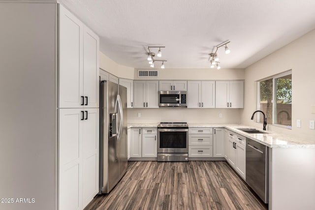 kitchen with light stone countertops, visible vents, a sink, stainless steel appliances, and dark wood-type flooring