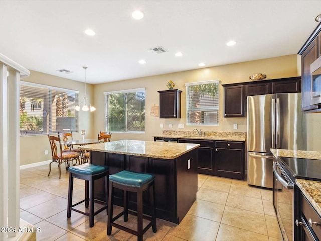 kitchen with dark brown cabinetry, appliances with stainless steel finishes, hanging light fixtures, and a kitchen island