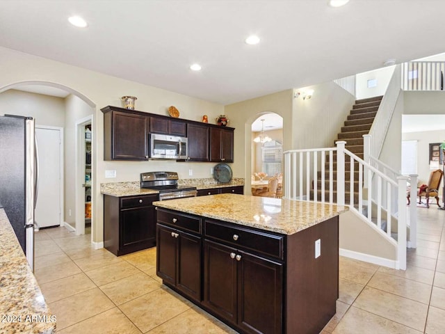 kitchen with light stone counters, stainless steel appliances, a kitchen island, dark brown cabinetry, and light tile patterned floors