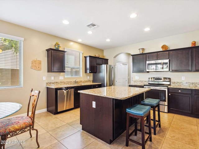 kitchen featuring a kitchen island, dark brown cabinetry, light tile patterned flooring, and stainless steel appliances