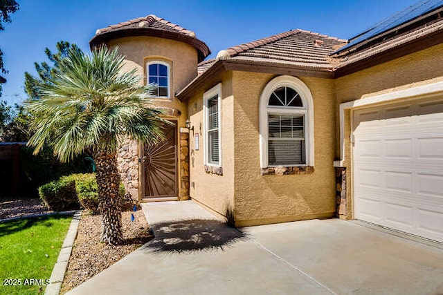 view of exterior entry featuring stucco siding, concrete driveway, a tile roof, and a garage