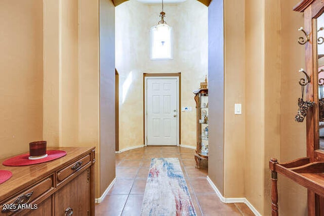 entryway featuring a high ceiling, light tile patterned floors, arched walkways, and baseboards