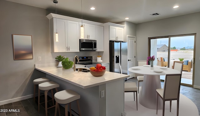 kitchen with a breakfast bar area, stainless steel appliances, decorative light fixtures, and white cabinetry