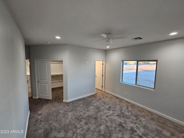 unfurnished bedroom featuring a closet, a walk in closet, dark carpet, and ceiling fan