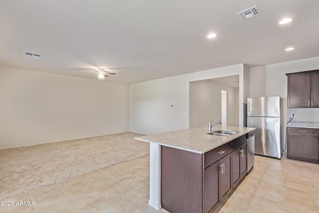 kitchen featuring dark brown cabinetry, sink, a kitchen island with sink, light carpet, and appliances with stainless steel finishes