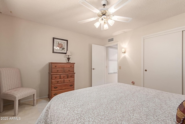 bedroom featuring ceiling fan, light colored carpet, a closet, and a textured ceiling