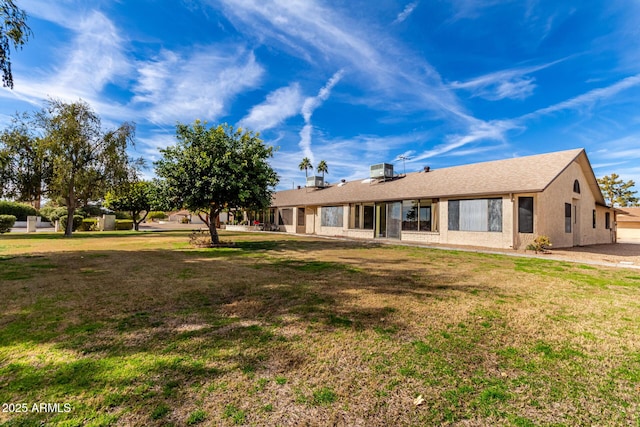 rear view of house with central air condition unit and a lawn