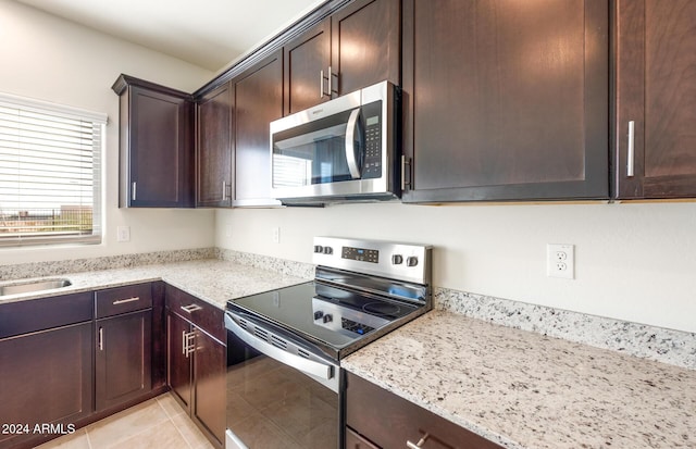 kitchen with dark brown cabinetry, light stone counters, light tile patterned floors, and stainless steel appliances