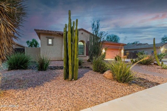 mediterranean / spanish-style home featuring an attached garage, a tile roof, and stucco siding