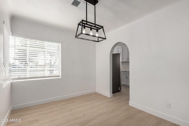 unfurnished dining area with visible vents, arched walkways, light wood finished floors, and baseboards