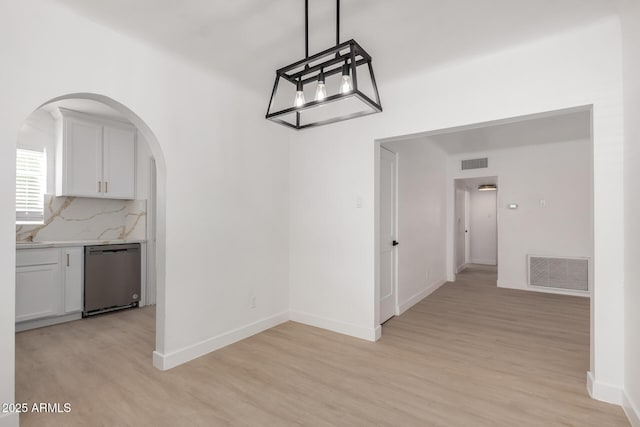 unfurnished dining area with light wood finished floors, visible vents, arched walkways, and baseboards