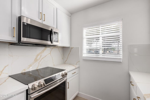 kitchen with backsplash, white cabinets, appliances with stainless steel finishes, and light stone counters