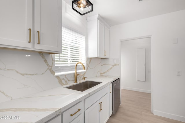 kitchen featuring a sink, light stone counters, decorative backsplash, white cabinetry, and stainless steel dishwasher