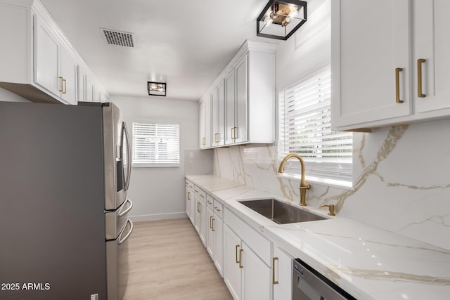 kitchen featuring visible vents, freestanding refrigerator, a sink, white cabinetry, and backsplash