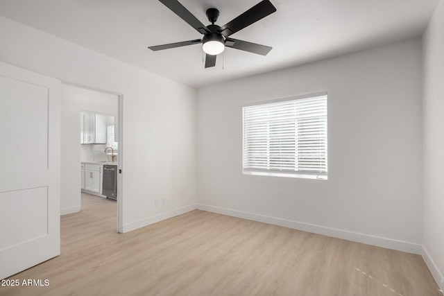 unfurnished room with baseboards, light wood-style floors, a ceiling fan, and a sink