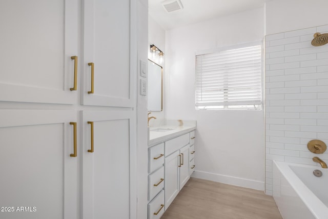 full bath with visible vents, wood finished floors, washtub / shower combination, baseboards, and vanity