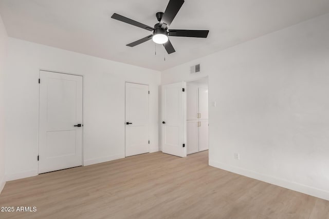 unfurnished bedroom featuring light wood-style flooring, baseboards, visible vents, and two closets