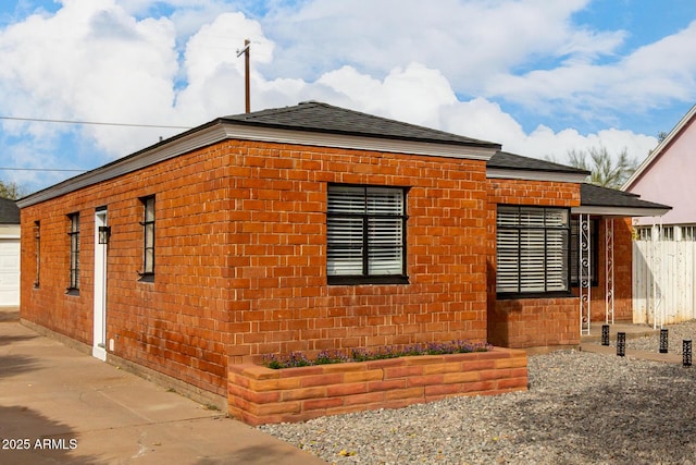 view of side of property featuring fence, brick siding, and roof with shingles